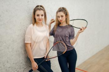 Two female players poses with squash rackets on court. Girls on game training, active sport hobby, fitness workout for healthy lifestyle
