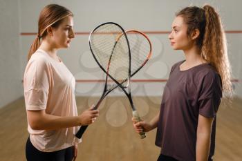 Two female players with squash rackets stands face to face. Girls on training, active sport hobby, fitness workout for healthy lifestyle