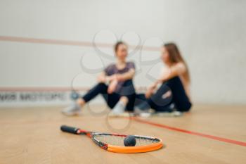 Two female players with squash rackets sits on court floor. Girls on training, active sport hobby, fitness workout for healthy lifestyle