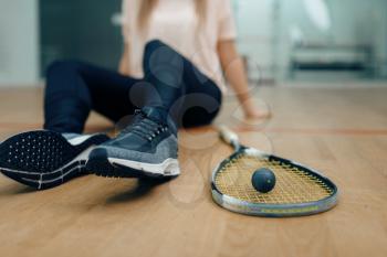 Female player with squash racket and ball sits on the floor. Girl on game training, active sport hobby on court