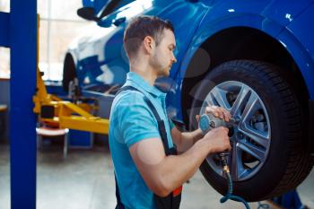 Worker in uniform removes wheel from vehicle on lift, car tire service station. Automobile checking and inspection, professional diagnostics and repair