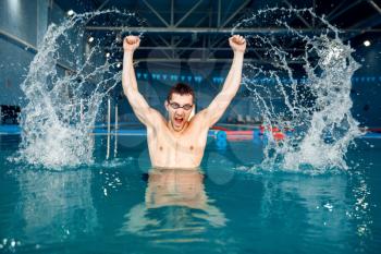Male swimmer in swimming glasses hits the water, the splashes rises up in pool, motion view. Sportsman at the poolside in the water
