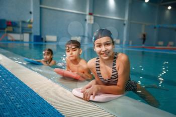 Children swimming group poses at the poolside. Kids learns to swim in the water, sport training in the pool
