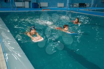 Children swimming group, workout in the pool. Kids learns to swim in the water, sport training, exercise with board