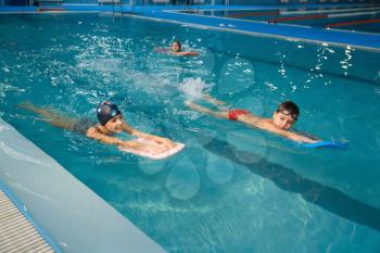 Children swimming group, workout in the pool. Kids learns to swim in the water, sport training, exercise with board