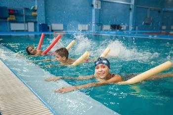 Children swimming group lies on back, workout in the pool. Kids learns to swim in the water, sport training, exercise with board