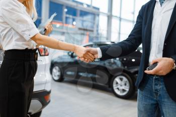 Man and saleswoman shake hands in car dealership. Customer and seller in vehicle showroom, male person buying transport, auto dealer business