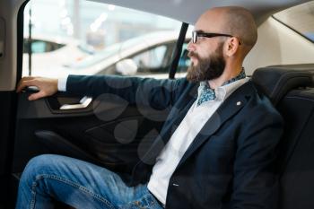 Man checks the comfort of rear seats in new automobile, car dealership. Customer in vehicle showroom, male person buying transport, auto dealer business