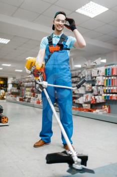 Male worker holds gas trimmer in tool store. Choice of professional equipment in hardware shop, electrical instrument supermarket