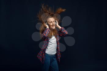 Little girl in headphones against powerful airflow in studio, developing hair effect. Children and wind, kid isolated on dark background, child emotion