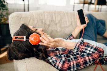 Woman in headphones listening to music on sofa. Pretty lady in earphones relax in the room, sound lover resting on couch