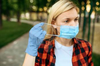 Young woman in gloves puts mask on her face in park, quarantine. Female person walking during the epidemic, health care and protection, pandemic lifestyle