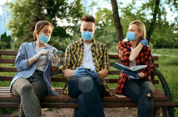 Young people in masks sitting on bench in park, quarantine. Female person walking during the epidemic, health care and protection, pandemic lifestyle