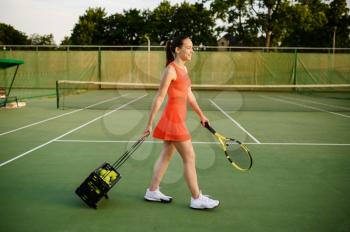 Female tennis player carries basket with balls on outdoor court. Active healthy lifestyle, sport game competition, fitness training with racquet