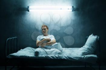 Sad psycho man sitting alone in bed, dark room on background. Psychedelic person having problems every night, depression and stress, sadness, psychiatry hospital