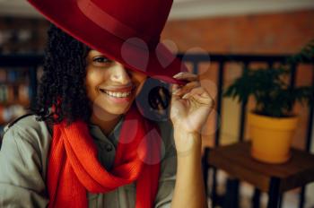 Pretty female student in red hat poses in cafe. Woman learning a subject in coffeehouse, education and food. Girl studying in campus cafeteria