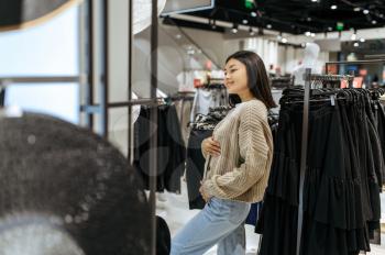 Young woman trying on cardigan in clothing store. Female person shopping in fashion boutique, shopaholic, shopper looking on garment