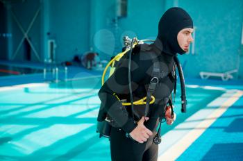 Male diver in scuba suit prepares for dive, diving school. Teaching people to swim underwater, indoor swimming pool interior on background
