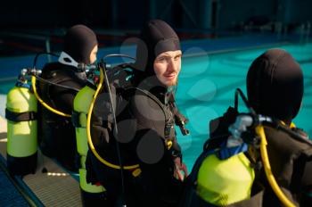 Divemaster and two divers in scuba gear preparing for the dive, diving school. Teaching people to swim underwater, indoor swimming pool interior on background