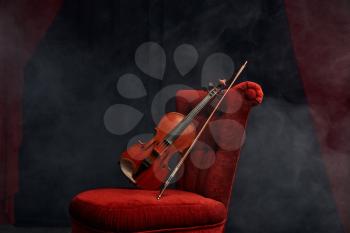 Violin in retro style and bow on the chair, nobody. Classical string musical instrument, music art, wooden viola, dark background