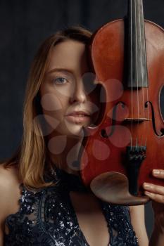 Female violonist with retro violin at her face. Woman with string musical instrument, music art, musician play on viola, dark background