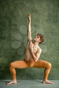 Male ballet dancer poses at grunge wall in dancing studio. Performer with muscular body, grace and elegance of movements