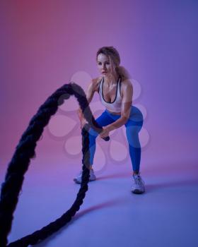 Young sportswoman with ropes poses in studio, neon background, crossfit. Fitness woman at the photo shoot, sport concept, active lifestyle motivation