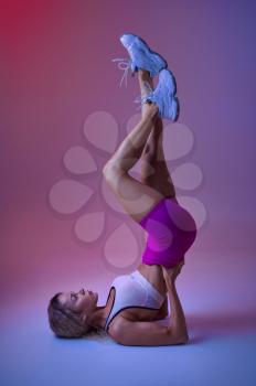 Sportswoman standing on her back in studio, neon background. Fitness woman at the photo shoot, sport concept, active lifestyle motivation
