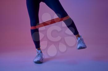 Sexy female athlete doing exercise with rubber in studio, neon background. Fitness sportswoman at the photo shoot, sport concept, active lifestyle motivation