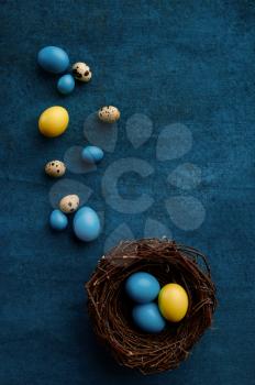 Easter eggs in decorative nest on blue cloth background. Paschal food, event decoration, spring holiday celebration symbol