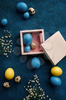 Easter eggs in gift box on blue cloth background. Spring wildflowers blooming and paschal food, fresh floral decoration for holiday celebration, event symbol