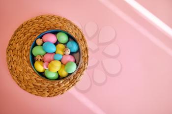 Colorful easter eggs in bowl, pink background, top view. Paschal food, event decoration, spring holiday celebration symbol