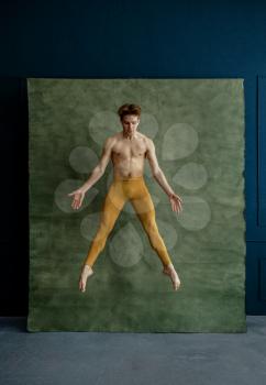 Male ballet dancer jumps in dancing studio, grunge wall on background. Performer with muscular body, grace and elegance of movements