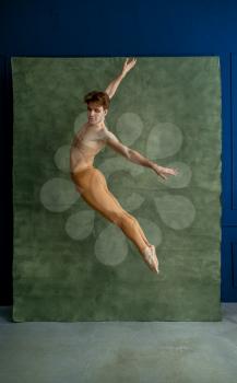 Male ballet dancer jumps in dancing studio, grunge wall on background. Performer with muscular body, grace and elegance of movements