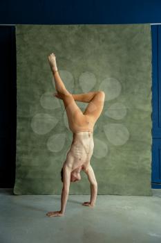 Male ballet dancer standing on hands, grunge wall on background, dancing studio. Dance performer with muscular body, grace and elegance of movements