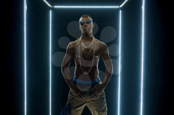 Serious rapper in gold chains dancing in illuminated cube, dark background. Hip-hop performer, rap singer, break-dance performing, entertainment lifestyle, breakdancer