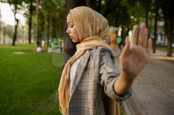 Arab girl in hijab shows her palm in summer park. Muslim woman with books resting on the lawn in university campus. Religion and education
