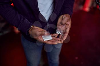 Drug addict man holds package of pills and powder in his hands, shebang interior on background, den. Narcotic addiction problem, eternal depression of junky people