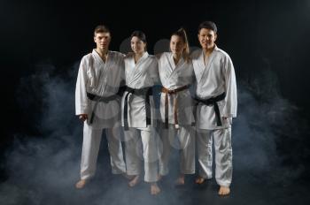 Four karate fighters in white kimono poses in a hug, group training, dark smoky background. Karatekas on workout, martial arts, fighting competition