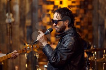Male singer in sunglasses at microphone, song performing on stage. Rock band performance, concert repetition in garage, live sound performer