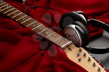 Electric guitar and headphones on red background, nobody. String musical instrument, electro sound, electronic music, equipment for stage concert