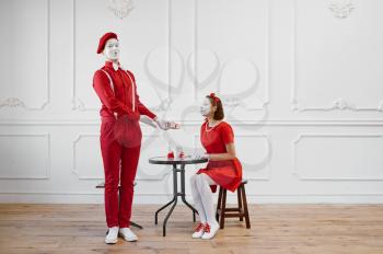 Two mime artists in red costumes, scene with gift. Pantomime theater, parody comedian, positive emotion, humour performance, funny face mimic and grimace