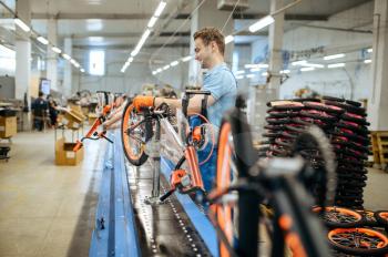 Bicycle factory, worker at assembly line, chain installation. Male mechanic in uniform installs cycle parts in workshop, industrial manufacturing