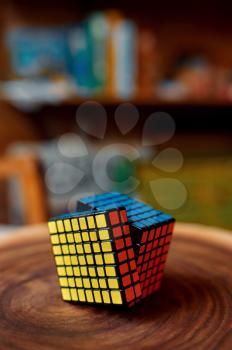 Colorful puzzle cube 7x7 on wooden stump, closeup view, nobody. Toy for brain and logical mind training, creative game, solving of complex problems