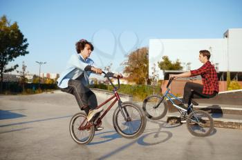 Two male bmx bikers doing tricks in skatepark. Extreme bicycle sport, dangerous cycle exercise, street riding, biking in summer park