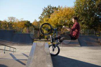 Young male bmx biker jumps on the wall in skatepark. Extreme bicycle sport, dangerous cycle trick, street riding, biking in summer park