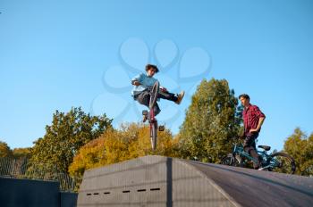 Two bmx bikers jumps on ramp, training in skatepark. Extreme bicycle sport, dangerous cycle exercise, street riding, biking in summer park