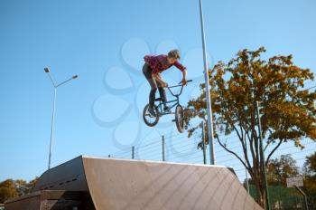 Male bmx biker jumps on ramp,teenager on training in skatepark. Extreme bicycle sport, dangerous cycle exercise, risk street riding, biking in summer park