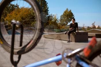 Young male bmx rider poses in skatepark at the bike. Extreme bicycle sport, dangerous cycle exercise, risk street riding, biking in summer park