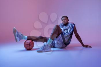 Basketball player poses with ball in studio, neon background. Professional male baller in sportswear playing sport game, tall sportsman